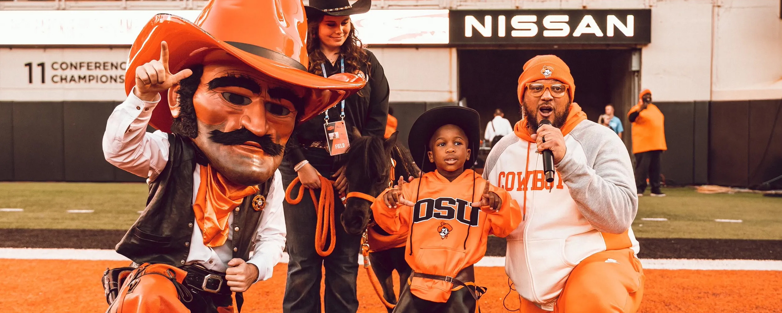 Pistol Pete, BB and handler, Warren the Cowboy and Les Thomas on the field in Boone Pickens Stadium. 