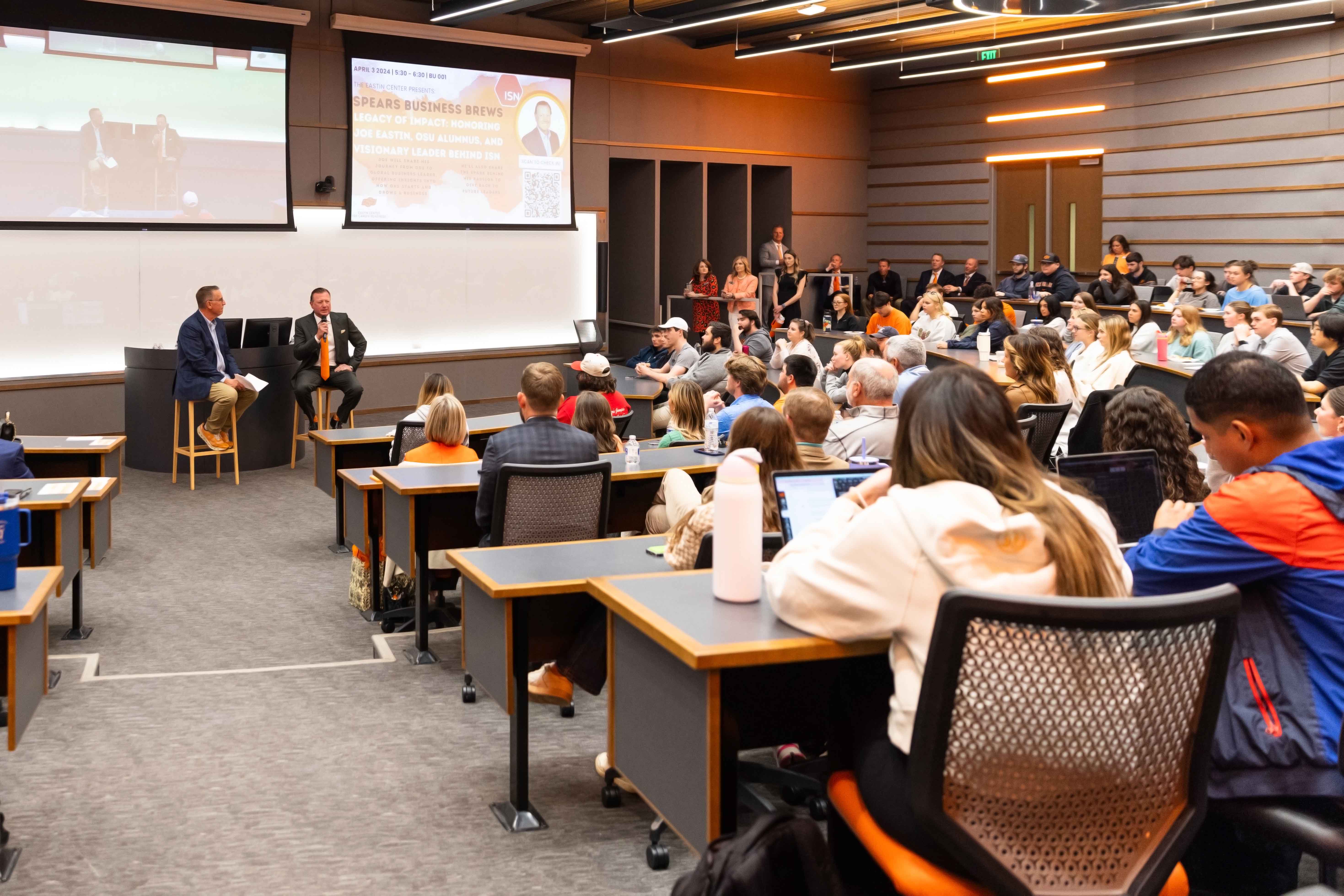 Speaker and moderator in front of a full classroom of students.