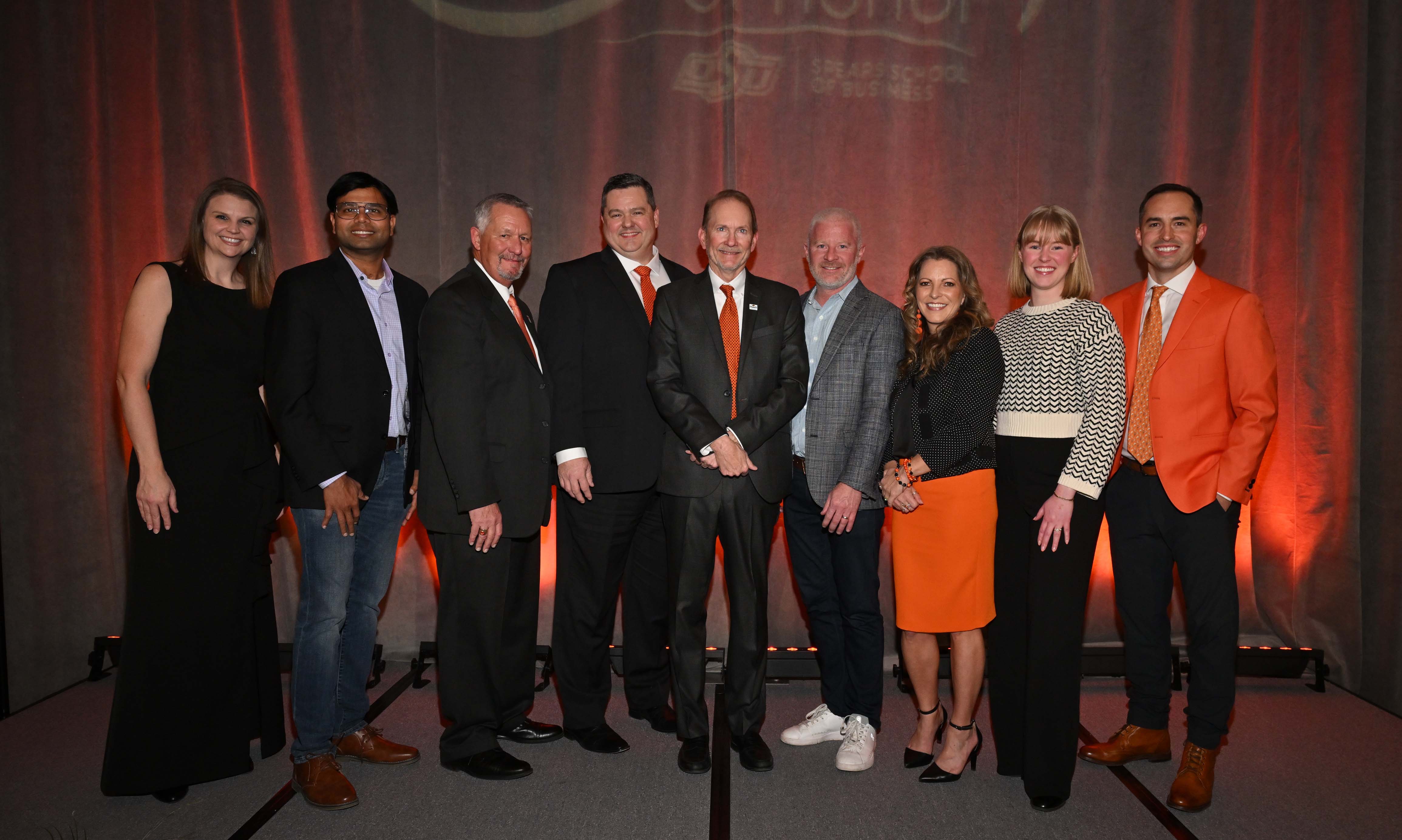 Group of alumni on a stage dressed in formal attire. Group of alumni on a stage dressed in formal attire.