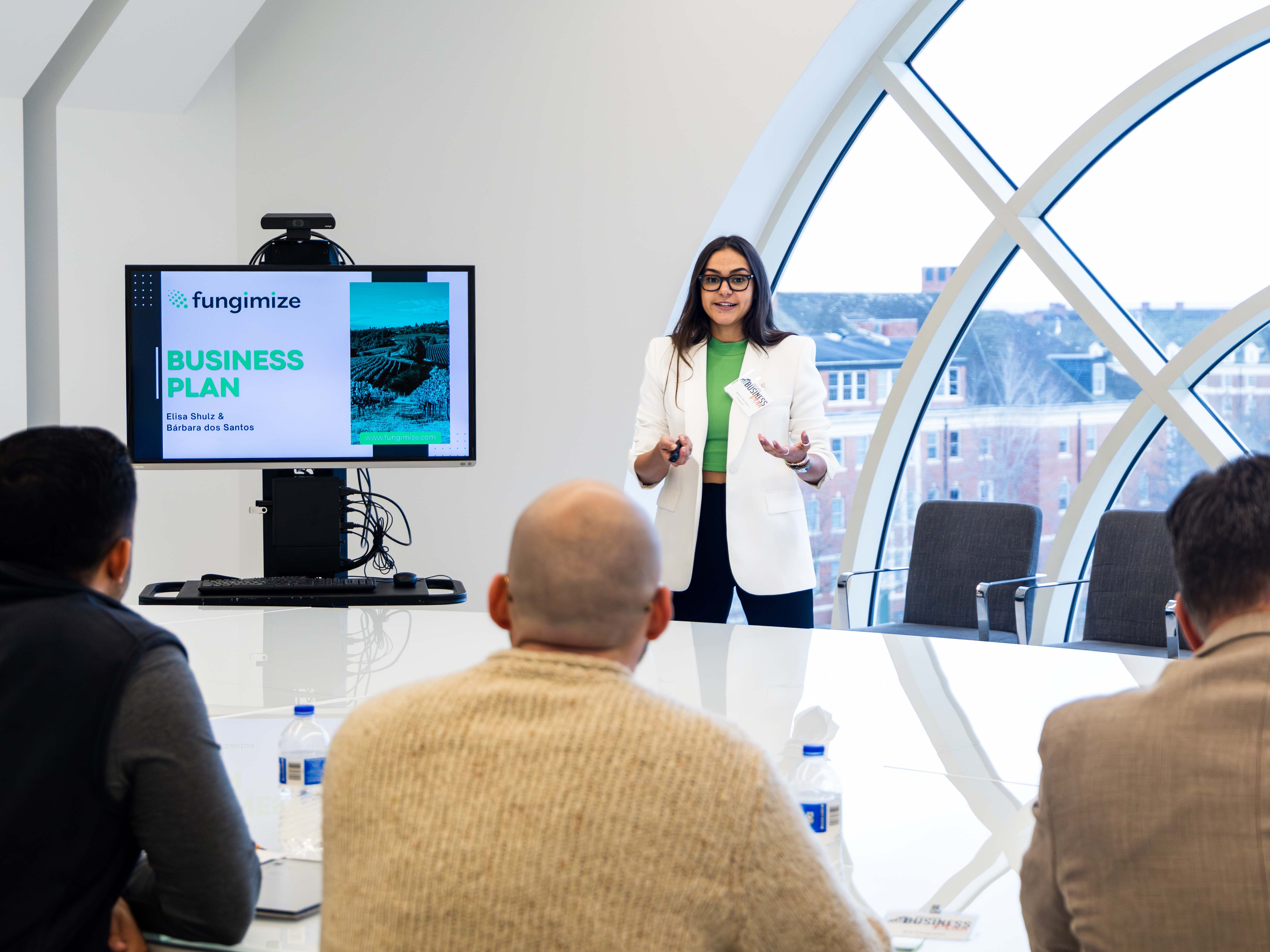 Female student giving a presentation wearing a white blazer and green top.